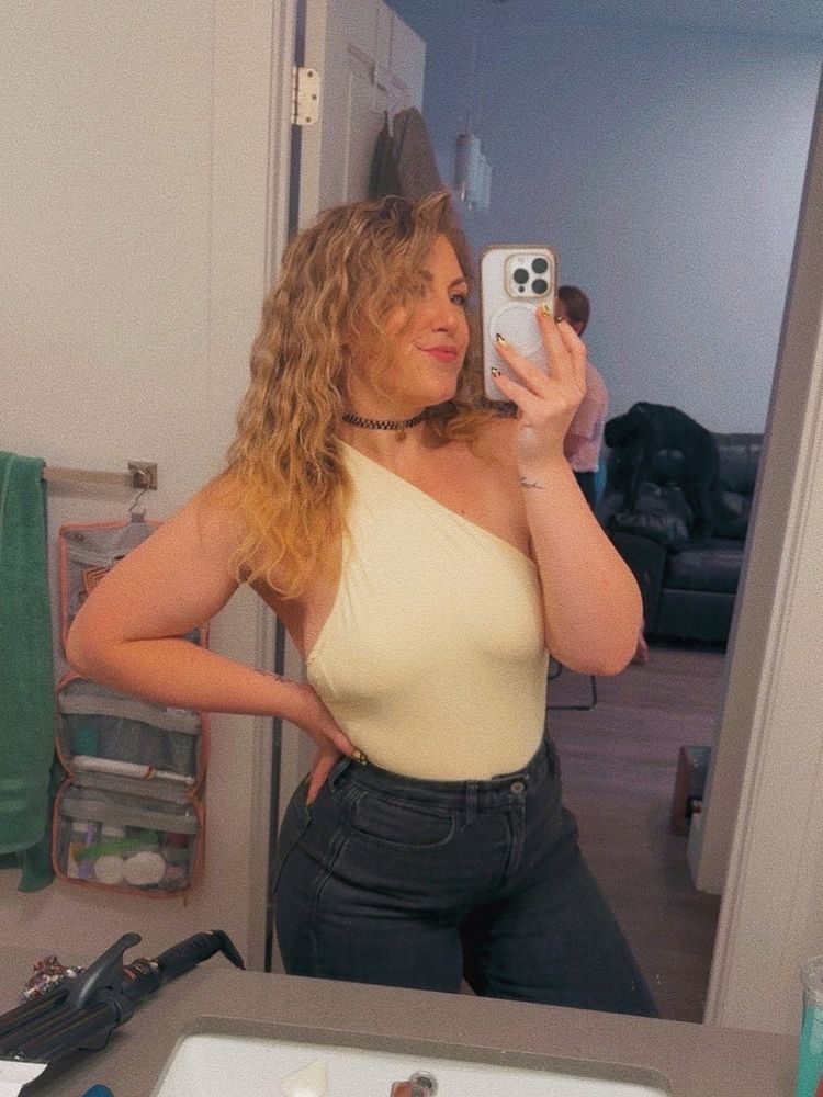 a woman taking a mirror selfie wearing black jeans and a yellow top 