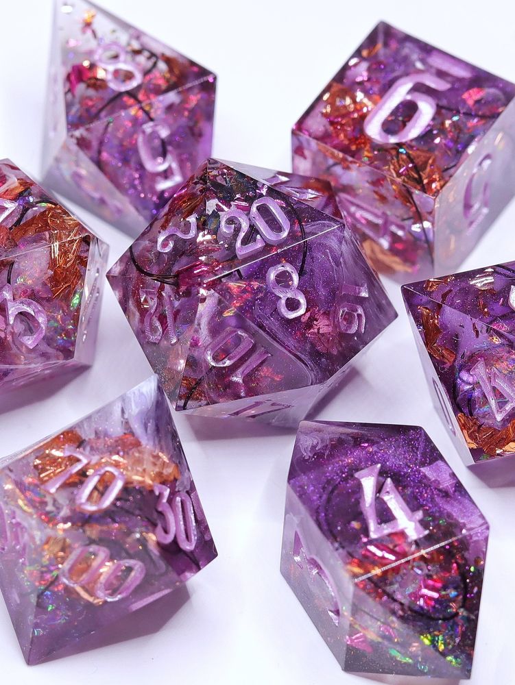 A set of 7 ttrpg dice. They are purple with pink and bronze foil, Holo foil, black wire, white swirls and pastel lilac numbers.