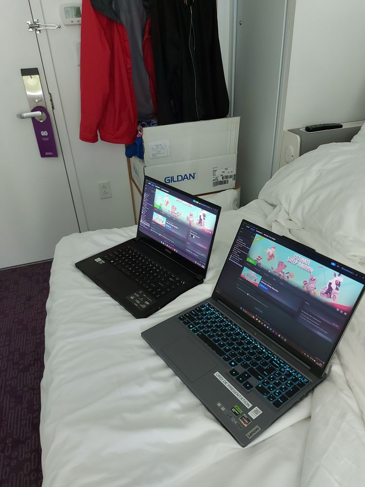 Image of two laptops sitting on the hotel bed showing the Steam page of our game, Ultimate Sheep Raccoon.