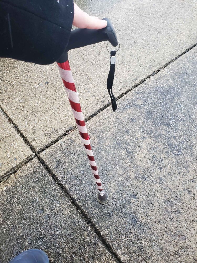 A photo of a person holding a cane. It's red with white stripes made of tape, so that it looks like a large candy cane