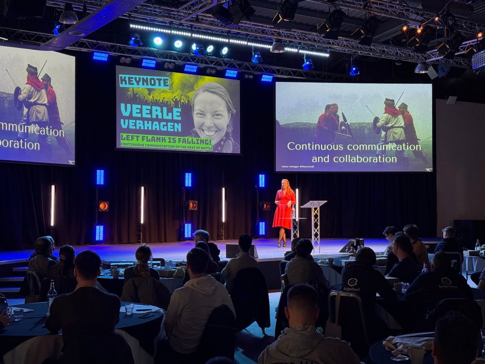 Speaker Veerle on stage at Testing Peers Conference. Images of Vikings on screen, and a quote about ‘Continuous communication and collaboration’