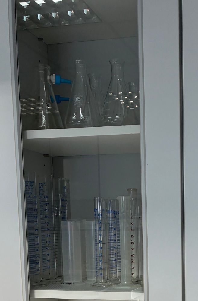 Das Foto zeigt eine Schranktür mit Glaseinsatz und auf den Schrankböden stehen verschiedene Laborgeräte.