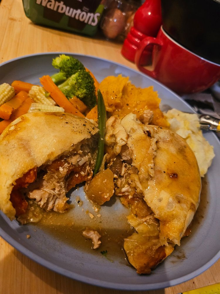 A cooked chicken casserole pie, split open and separated to show the filling, with a small amount of mashed potato, mashed swede and carrots, plus a mix of vegetables (carrots, broccoli, baby corn etc).