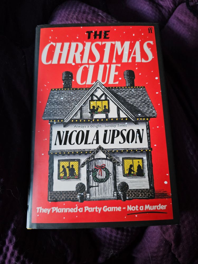A red boulder book with a whimsical house, with a Christmas wreath in the door, snow falling around it, and dark figures in the windows. 
The text reads:

THE CHRISTMAS CLUE

Always a delight. Sunday Times

NICOLA UPSON

They Planned a Party Game - Not a Murder