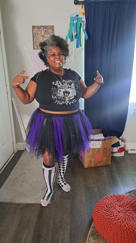 A black woman in a purple and black petticoat, black shirt and fairy wings