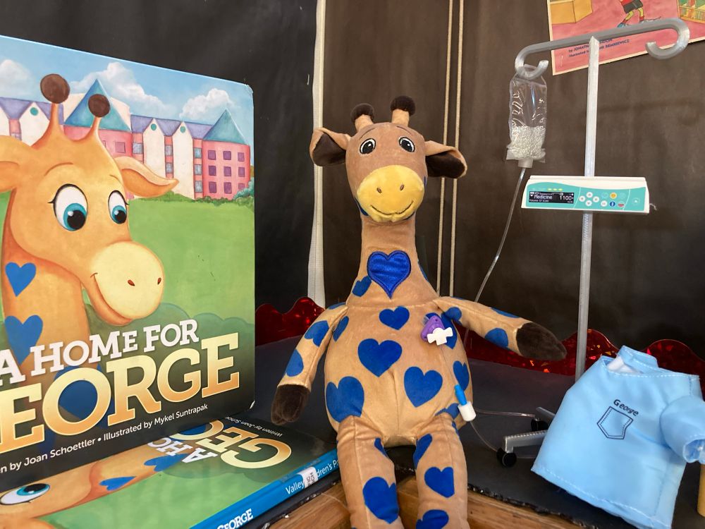 The book “A Home for George” about Valley Childrens Hospital, pictured with a stuffie of their giraffe mascot, while he’s having chemo using a toy induction pump by TheButterflypig.com. 