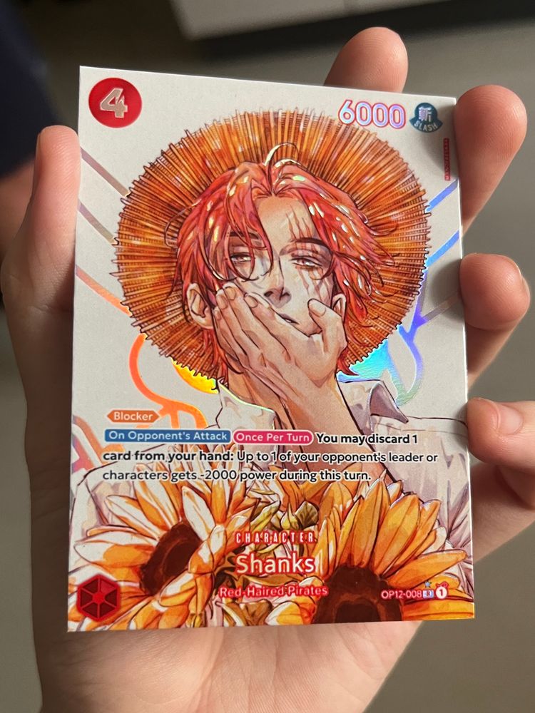 photo of a fanmade custom one piece card. art is of a young shanks with two sunflowers covering his chest and going off-card. there is a holographic effect of his jolly roger. the art has a watercolour effect.