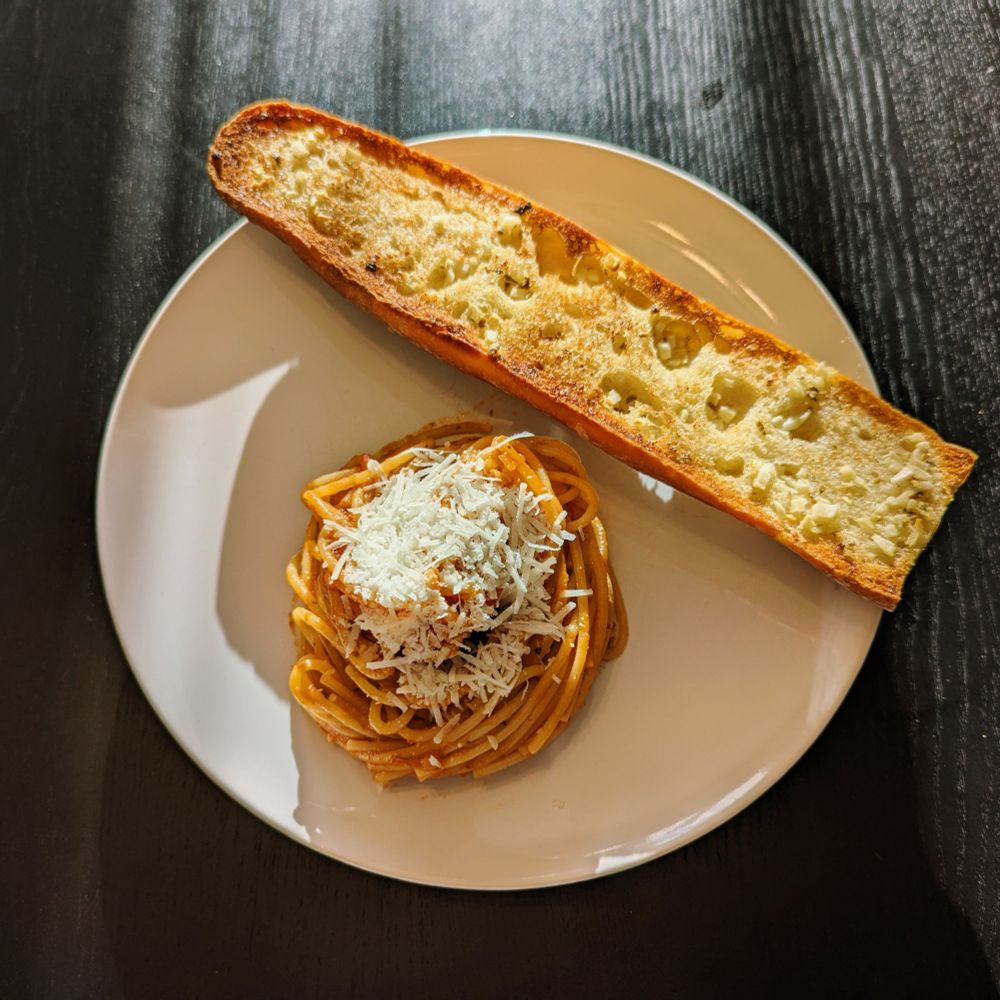 A plate of spaghetti and half a baguette of garlic bread, seen from above
