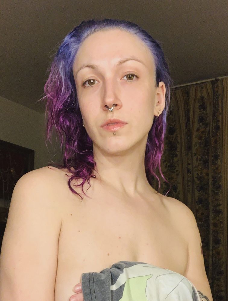 Lady with damp pink and blue hair hiding her breast with an arm.