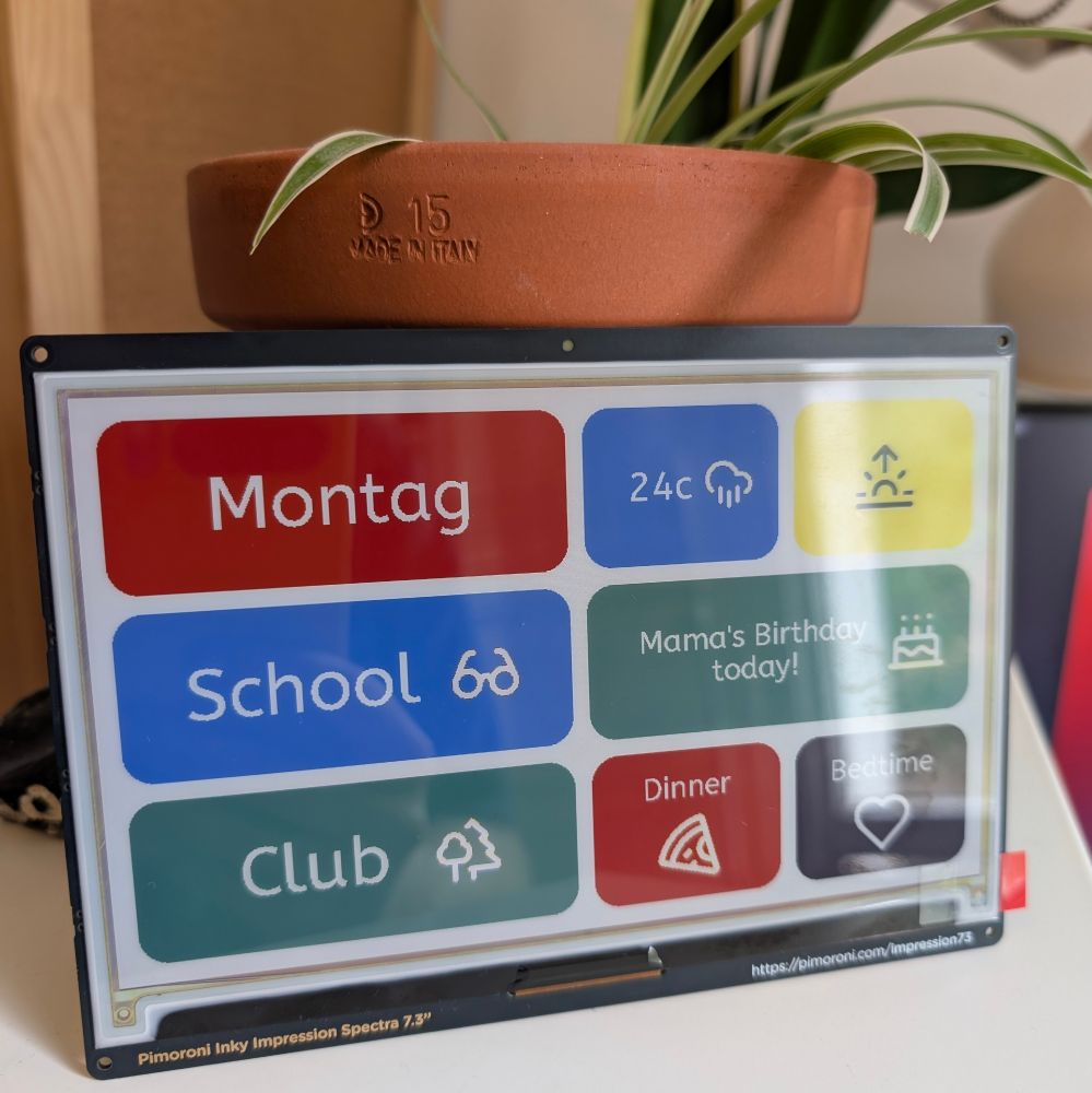 A Pimoroni Inky Impression Spectra 7.3" e-paper display shows a vibrant daily schedule with "Montag," "School," "Club," "24°C" weather, "Mama's Birthday today!", "Dinner," and "Bedtime" in colored boxes. A plant in a terracotta pot sits atop the display.