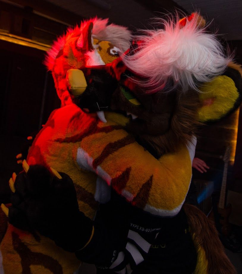 Tiger fursuit hugging the pine marten Virne under a red light.