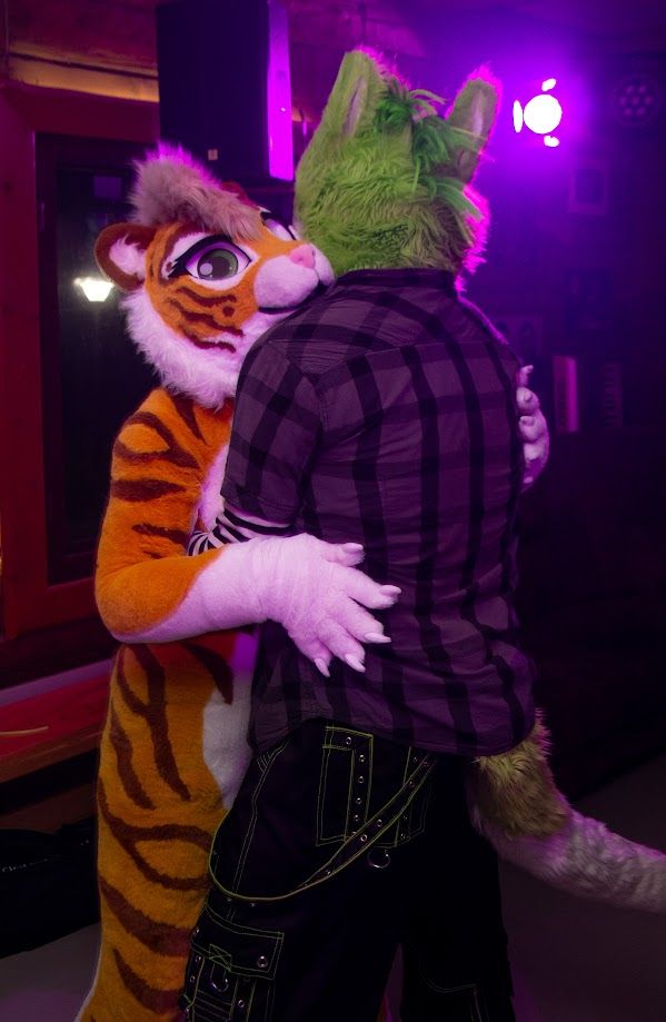 Tiger fursuiter hugging a sergal fursuiter on the dance floor.
