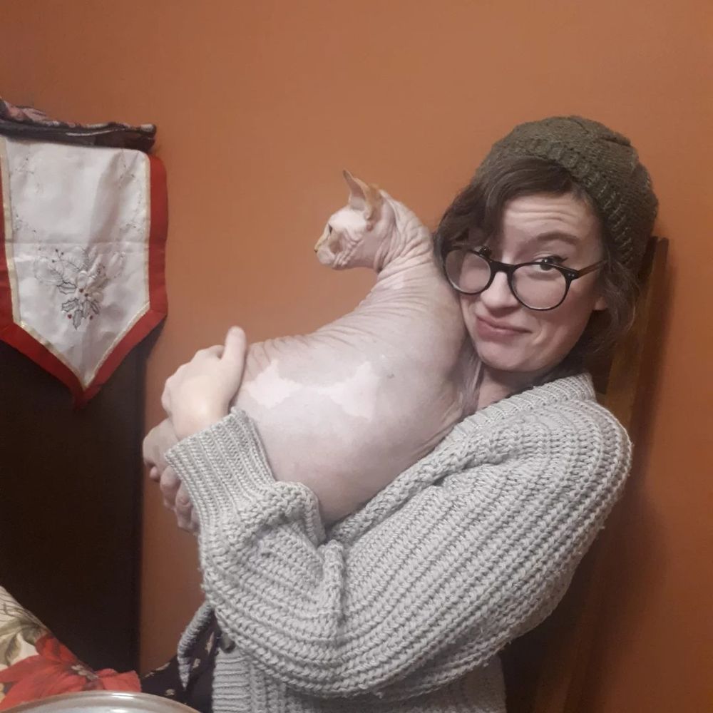bespectacled woman in knitwear holding a hairless cat