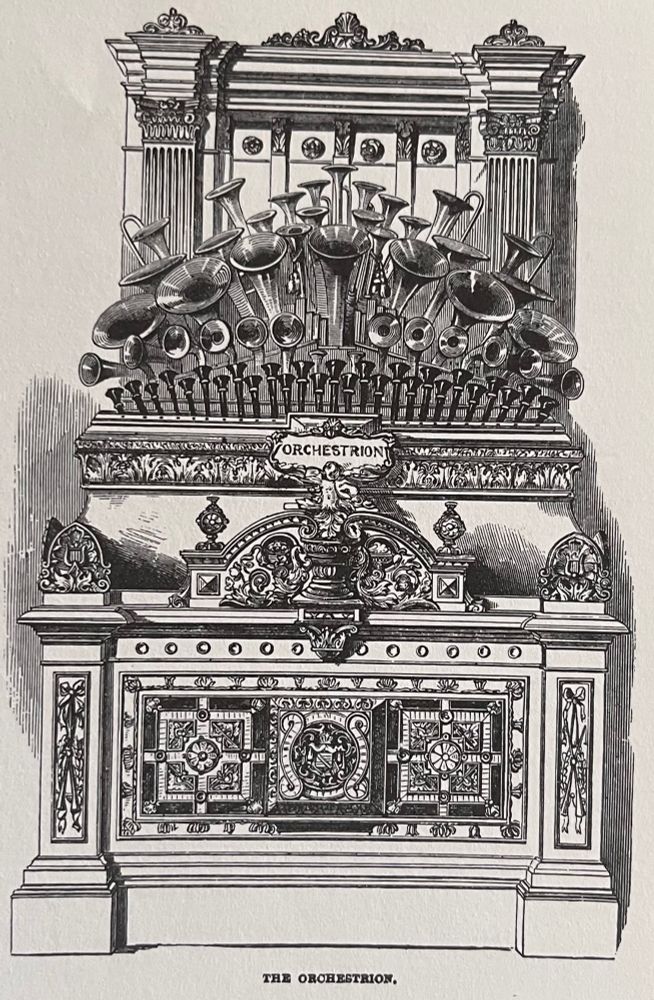 Detailed black-and-white engraving of a large ornate mechanical musical instrument labeled “Orchestrion.” The machine is decorated with elaborate architectural and floral carvings. A prominent array of brass horns and pipes emerges from the upper section, suggesting a combination of organ, wind, and percussion elements. The lower half resembles a carved cabinet with intricate geometric and floral designs. The word “ORCHESTRION” is displayed on a central sign above a carved figure. The caption below the image reads: “THE ORCHESTRION.”