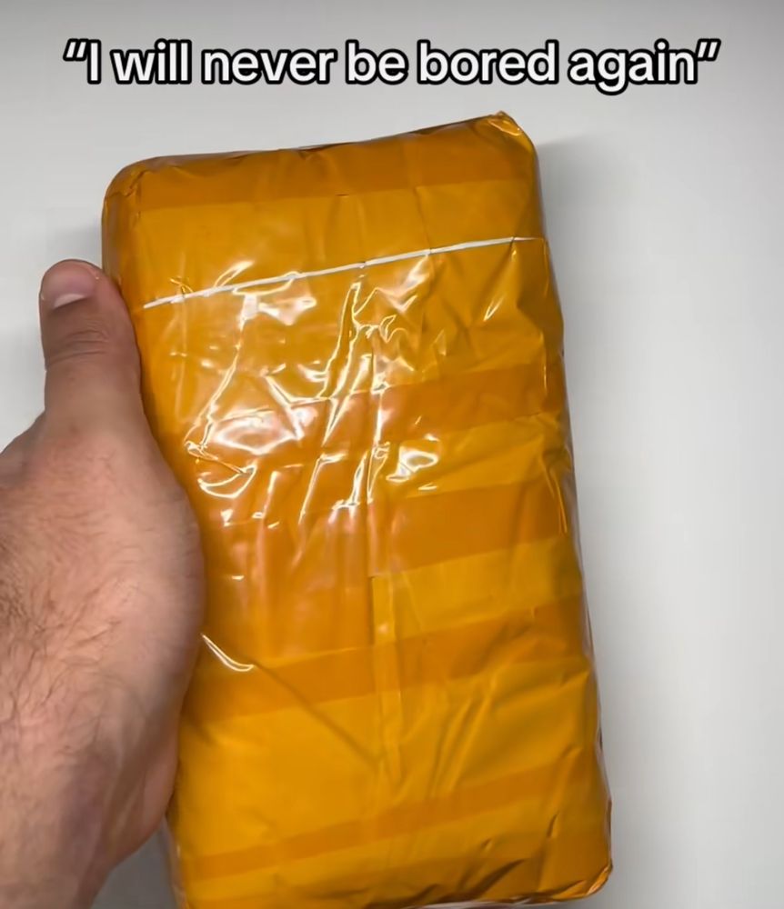 A hand holding what looks like a taped up brick of cocaine with the words “I’ll never be bored again” above it. 