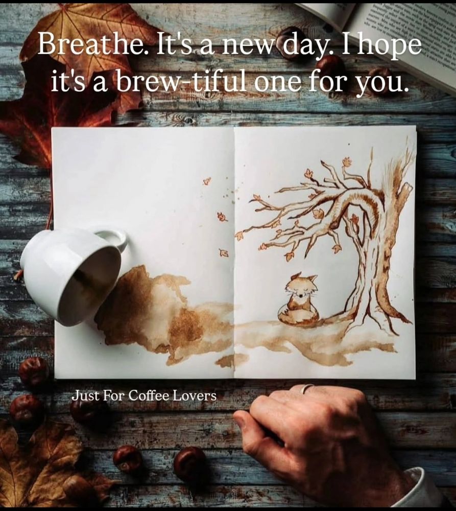 Auf einem hölzernen Tisch liegt ein aufgeschlagenes Skizzenbuch mit einer Zeichnung eines Baumes und eines kleinen Tieres, das darunter sitzt. Neben dem Buch liegt eine umgekippte weiße Kaffeetasse, aus der eine kaffeefarbene Flüssigkeit ausgelaufen ist und sich auf der Seite des Buches verteilt hat. Um das Buch herum liegen einige Kastanien und ein großes, braunes Herbstblatt. Eine Hand mit einem weißen Hemdärmel ist am unteren Bildrand zu sehen. Über dem Buch steht in weißer Schrift: 'Breathe. It's a new day. I hope it's a brew-tiful one for you.' Unter dem Buch steht in kleinerer weißer Schrift: 'Just For Coffee Lovers'.
