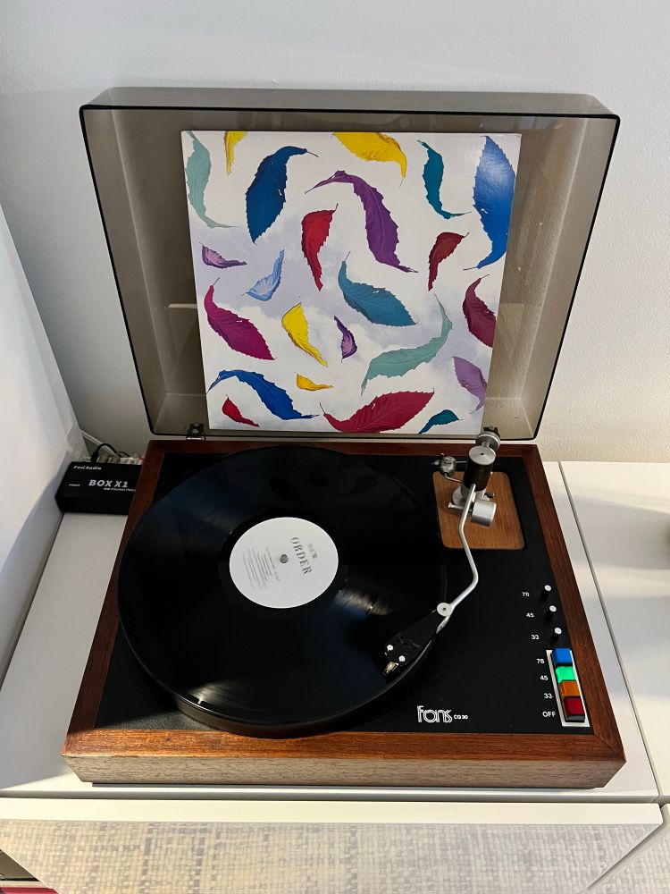 A 12” single of New Order’s “True Faith - Remix” is playing on a vintage FONS turntable. 