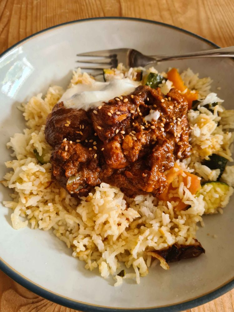 slightly blurry photo of a dish full of very delicious chicken tikka, atop courgette and halloumi fried rice. the dish is finished with some yogurt and a sprinkling of sesame seeds.