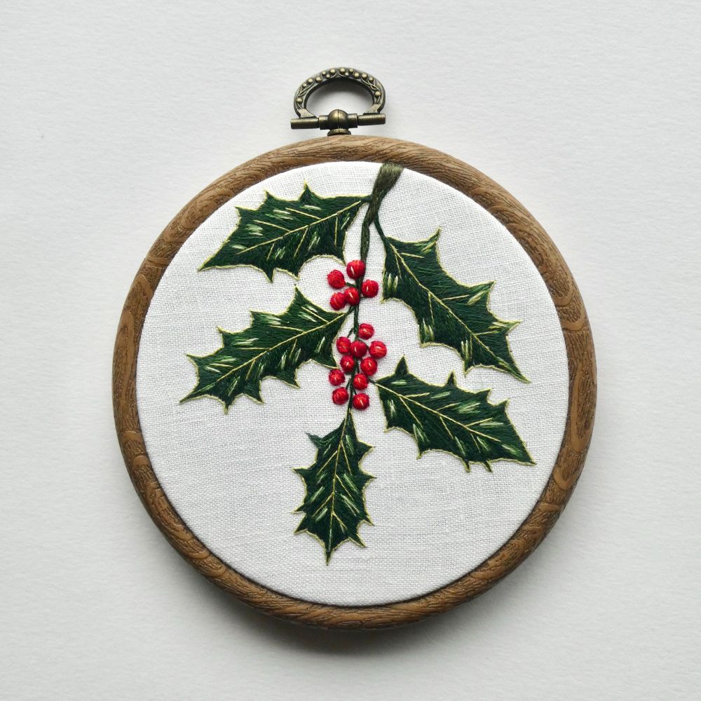 Embroidery hoop with white fabric and embroidery of holly with red berries