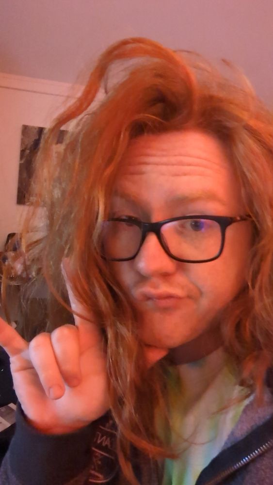 A picture of me with messy hair making the ASL hand sign for I love you, with my thumb somewhat hidden under my hair and chin