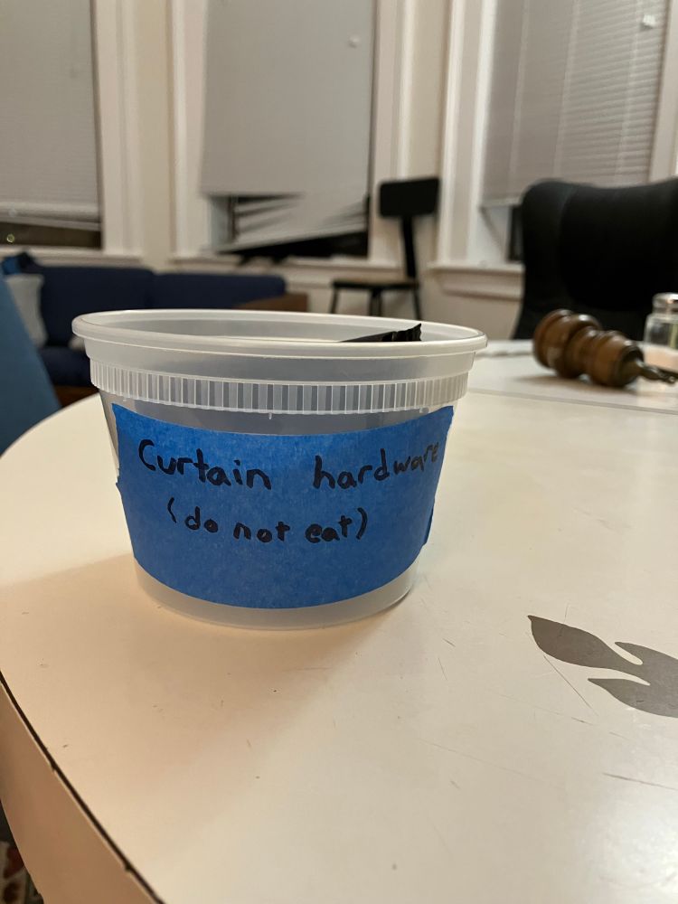 Plastic food container with blue label: “curtain hardware (do not eat)”