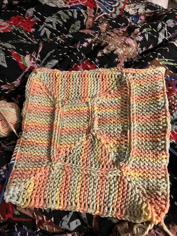 A square spiral piece of knitting using Frankie Brown’s Ten Stitch Blanket pattern. Slipped stitches along the spiral create a look of a U in a square. 