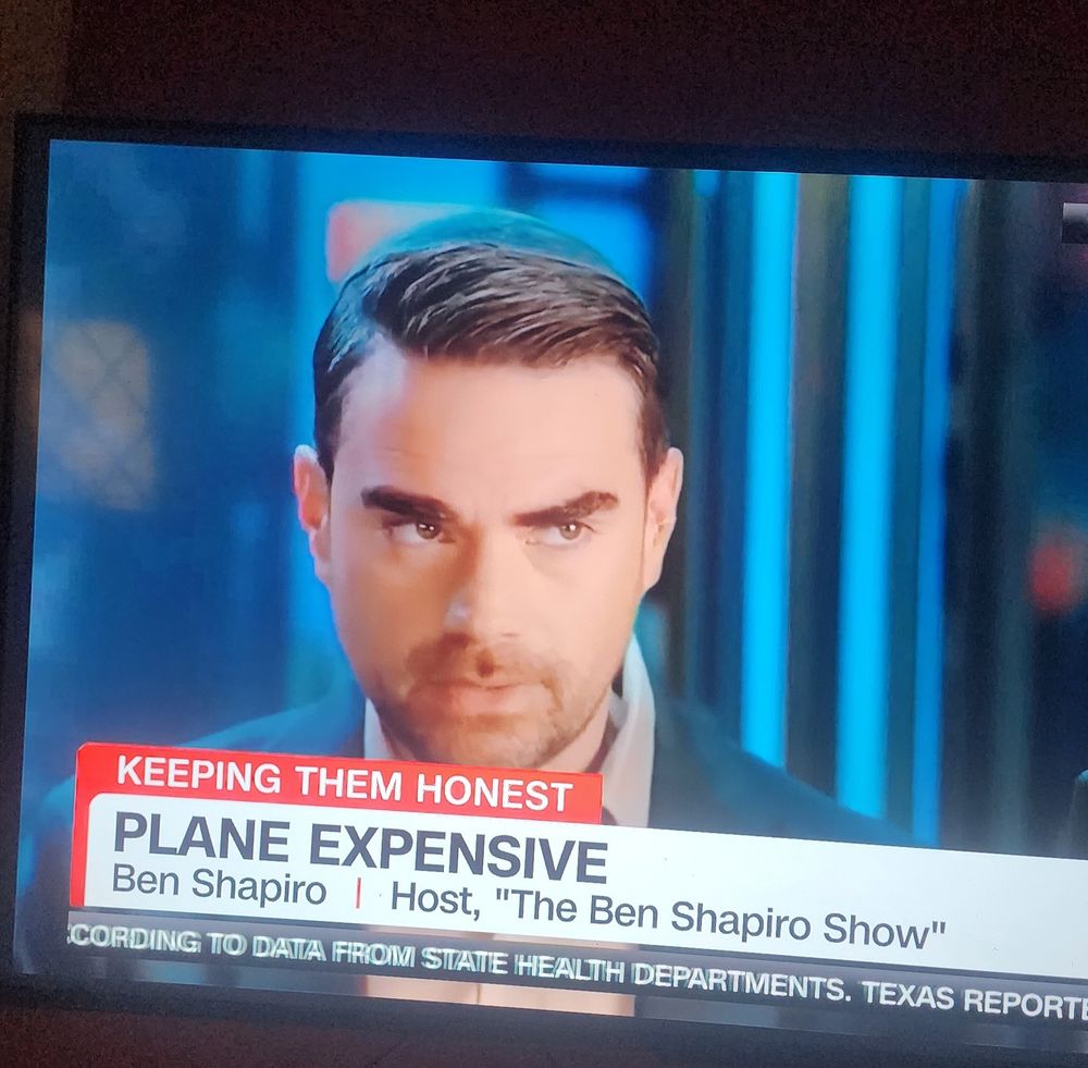 TV image of Ben Shapiro with a "evil" look on his face on CNN with a headline about Trumps gift from Qatar that says "Plane Expensive". 