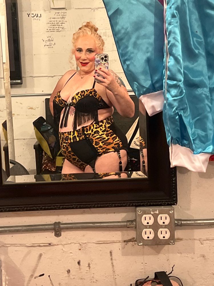 In black and leopard lingerie, into a mirror with a blue costume hanging alongside 