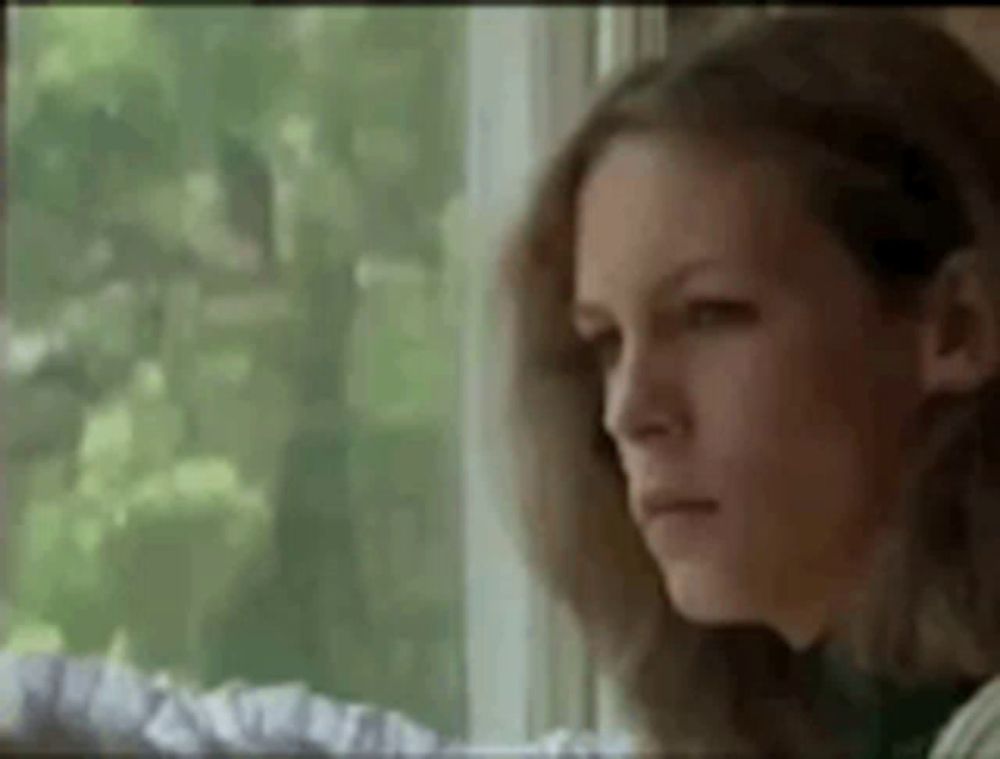 a woman is looking out a window with a sad look on her face .