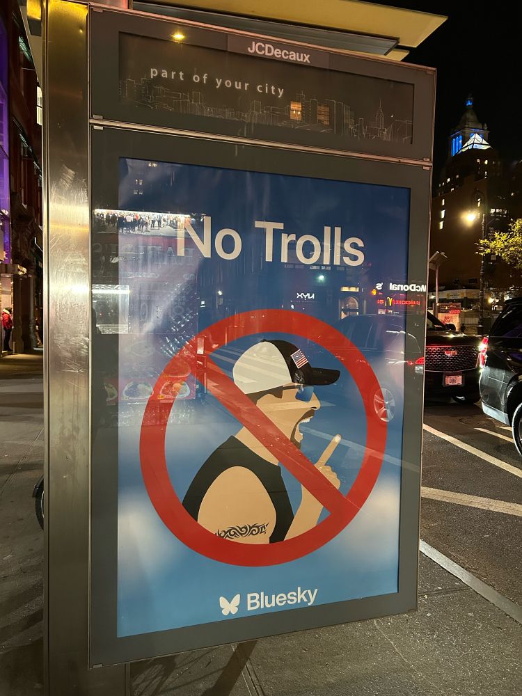 An ad for Bluesky in New York City that says “No Trolls” with a man wearing a USA hat in a 🚫 symbol
