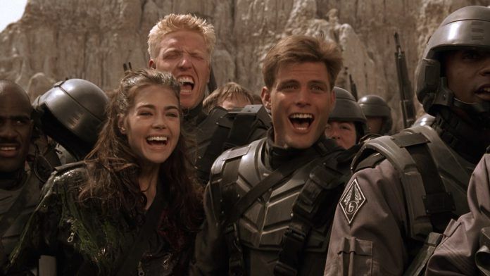A shot from Starship Troopers of Denise Richards, Jake Busey, and Casper Van Dien celebrating their victory over the “brain bug”