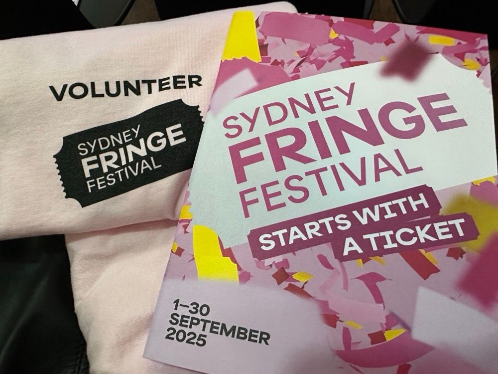 A pink brochure for the Sydney Fringe Festival, alongside a pink Fringe Festival Volunteer t-shirt