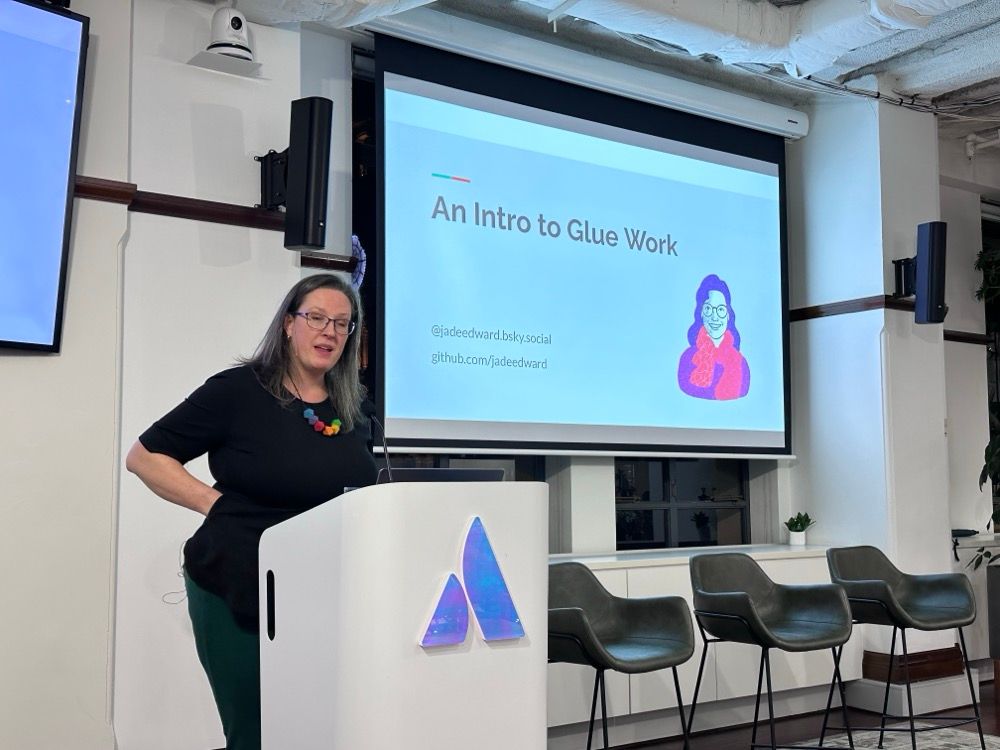 A woman presenting at a tech event with a slide that says "An Intro to Glue Work"