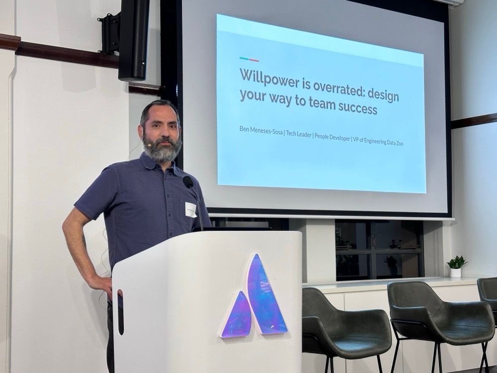 A man presenting at an event with a slide that says "Willpower is overrated: designer your way to team success"