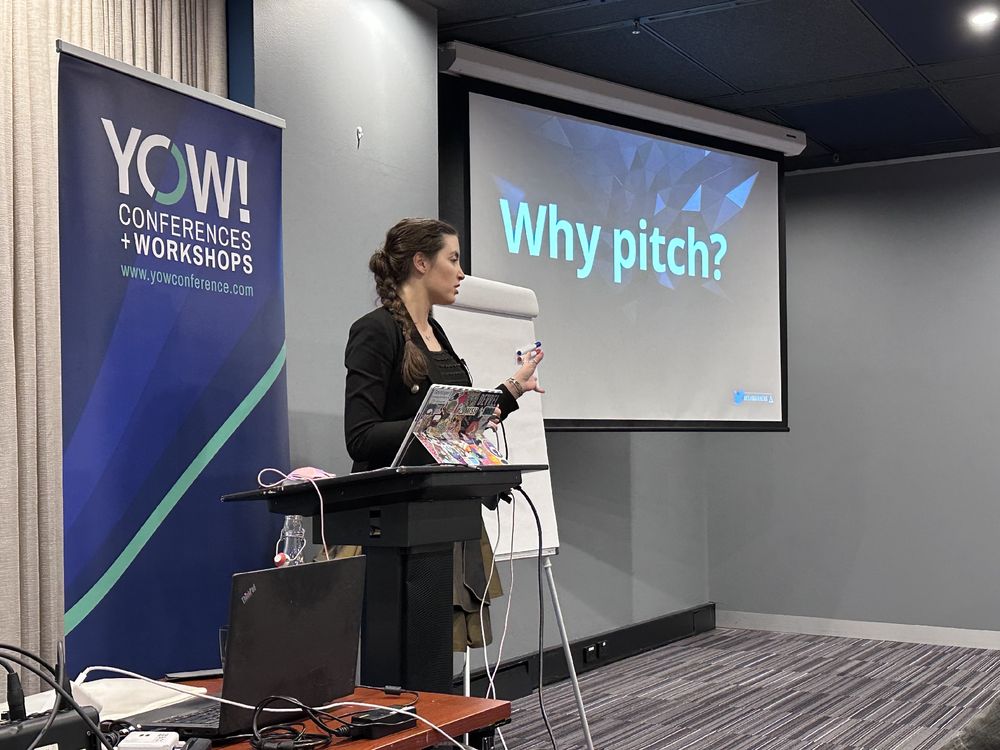A woman presenting at a tech event, with a slide that says WHY PITCH?