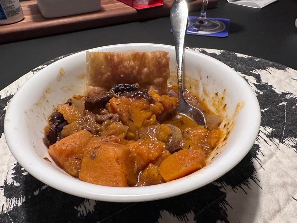 A bowl of stew with pork, sweet potatoes and prunes, with a piece of focaccia