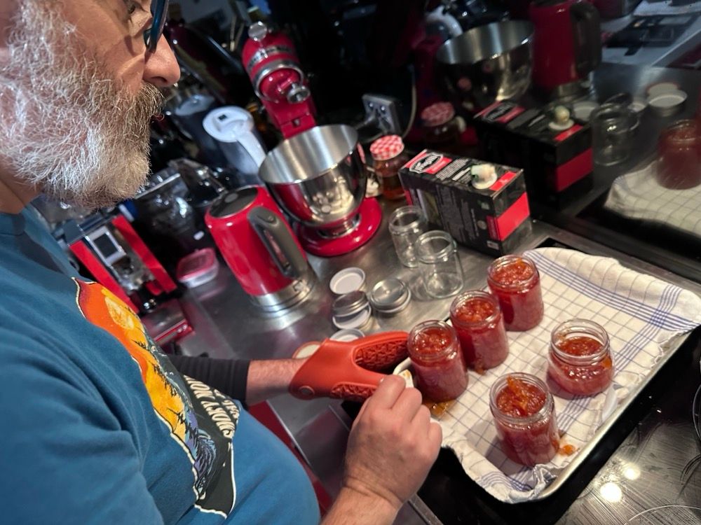 A bearded man spooning jam in jars
