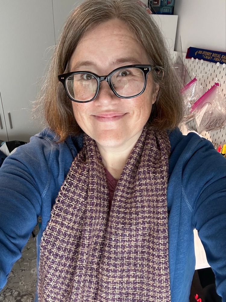 A woman in glasses wearing a blue hoodie and a purple/camel houndstooth woven wool scarf