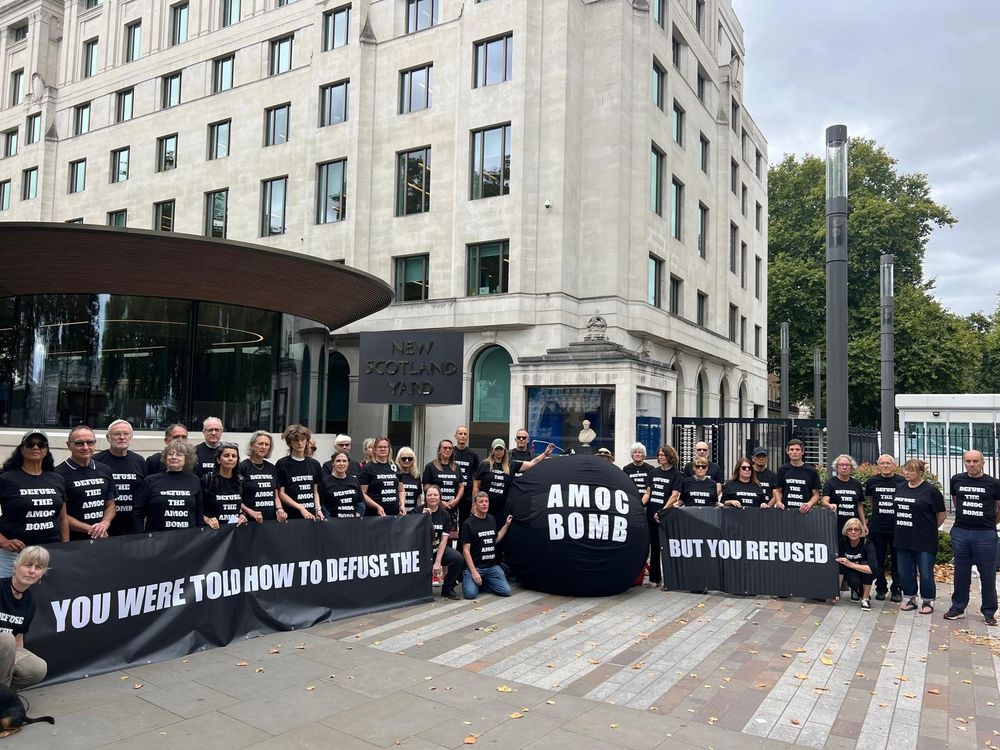 protestors carry banners and a bomb outside New Scotland Yard saying "YOU WERE TOLD HOW TO DEFUSE THE AMOC BOMB BUT YOU REFUSED"