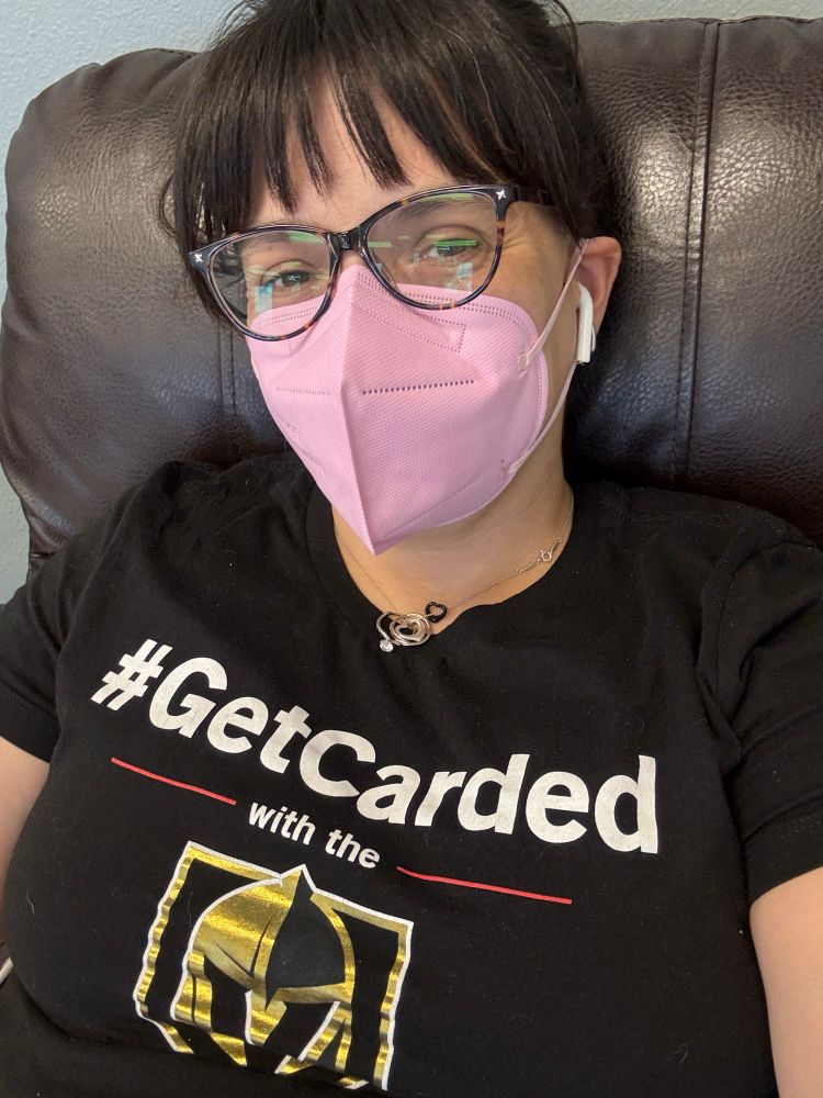 Masked woman wearing a golden knights #GetCarded shirt