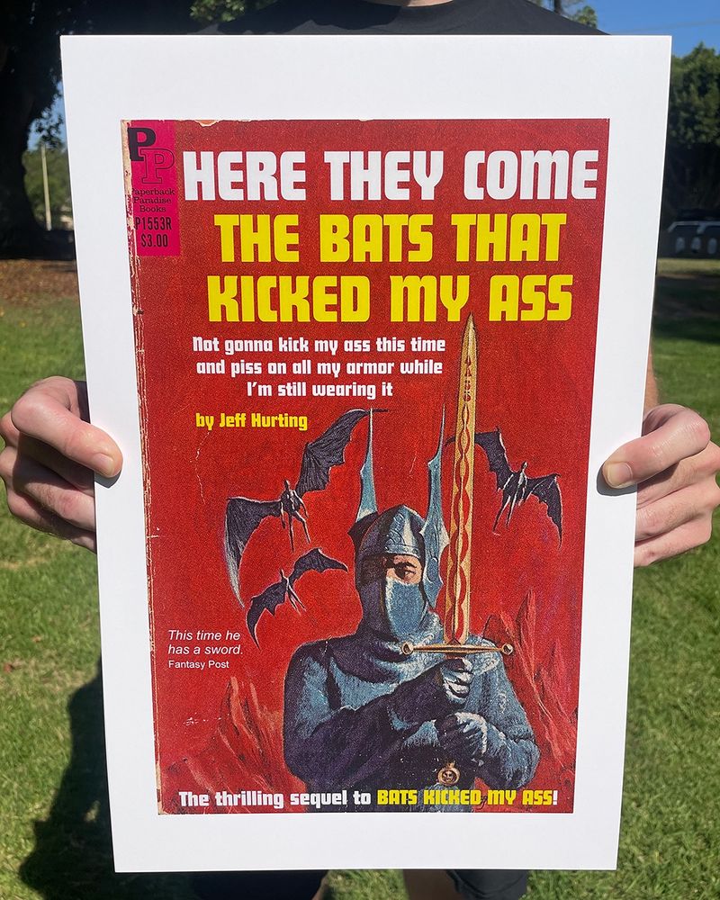 Photo of a print being held up on a bright summer day, print features the paperback paradise book Here They Come: The Bats That Kicked My Ass