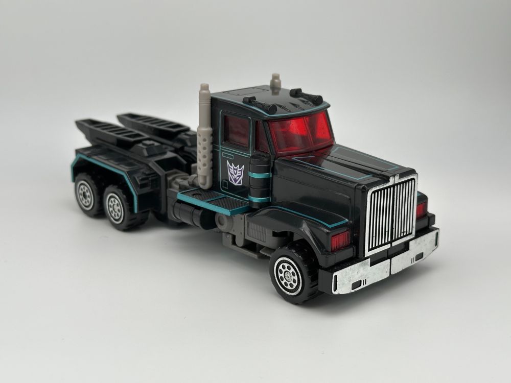 a toy of a black long-nosed truck with red windows and some teal highlights 