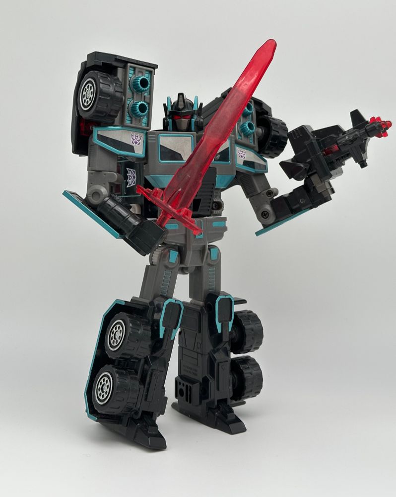 a toy of a gray, black, and teal robot carrying a sword and a gun, against a white background