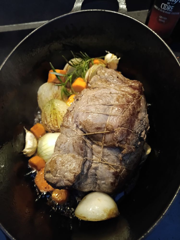 Cocotte contenant le rôti bien doré, les oignons, carottes, gousses d'ail et romarin en train de dorer