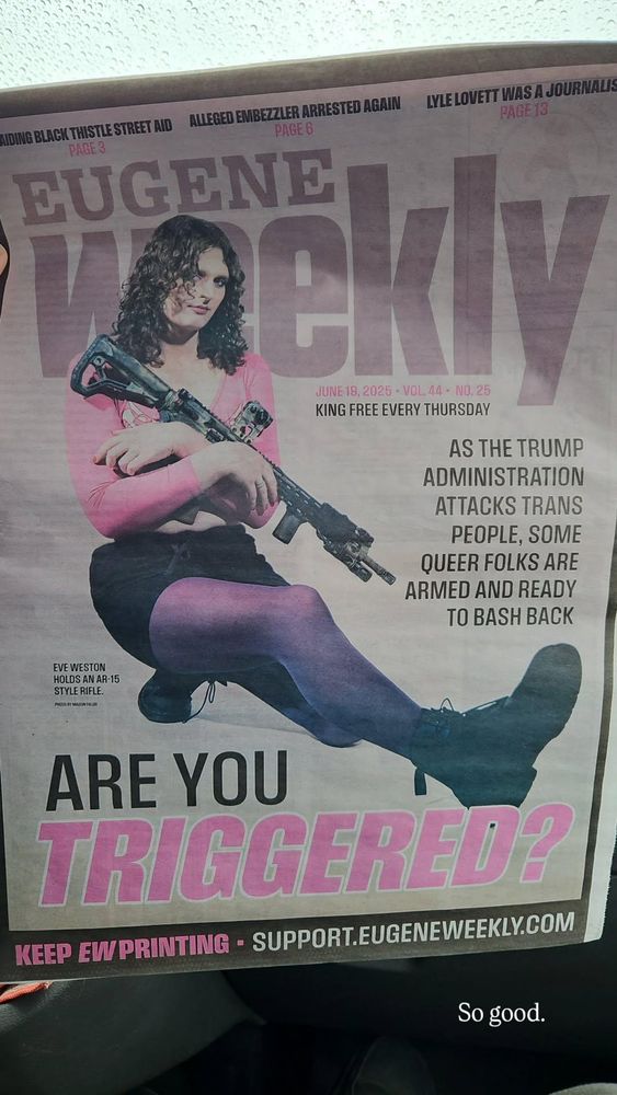 The cover of Eugene Weekly featuring a devastatingly hot woman holding an AR15 with the headline "ARE YOU TRIGGERED." The subheading says "as the Trump administration attacks trans people, some queer folks are armed and ready to bash back." Cover model is Eve Weston. She is wearing a pink crop top, black mini skirt, purple tights, and combat boots as she cradles the AR15. The title of the alt weekly "Eugene Weekly" is in purple and the "triggered" in "Are you triggered" is pink. It is hard to express in my little words how hard this goes.