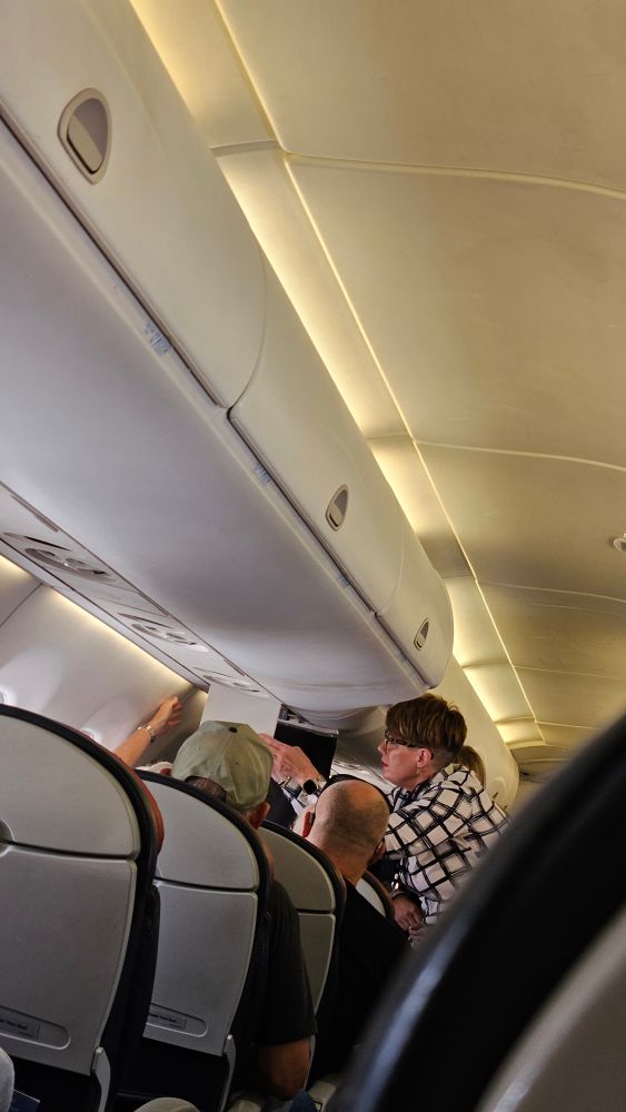 Flight attendant trying to fix the oxygen mask panel that is broken and dangling.