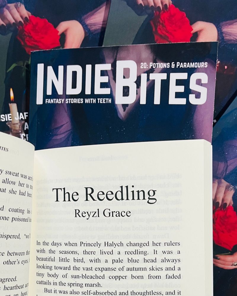 Indie Bites 20 open to the title page of Reyzl’s story, on a stack of copies showing the cover.