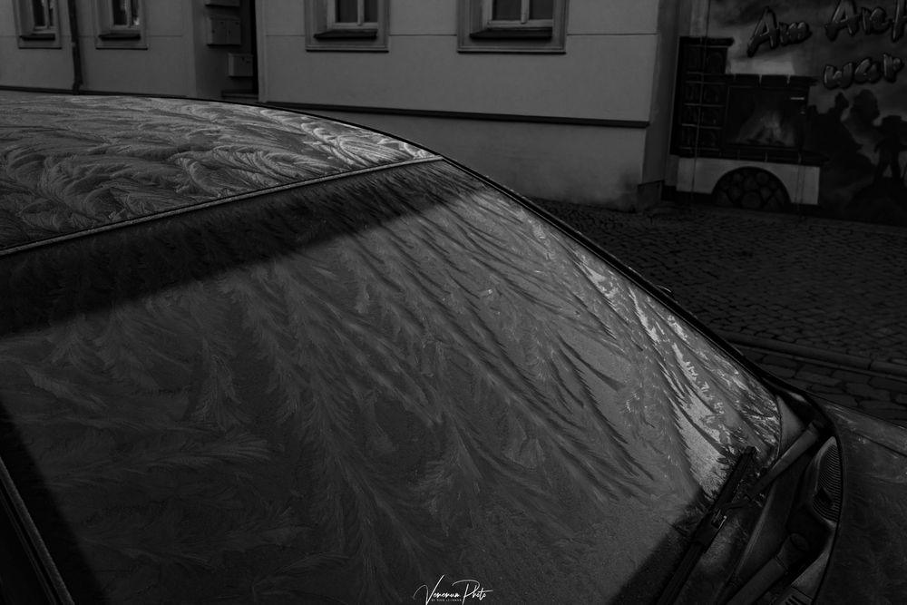 Schwarzweißbild eines geparktem Auto in einer kleinen Straße in einer Stadt, gefrorene Frontscheibe und Autodach 