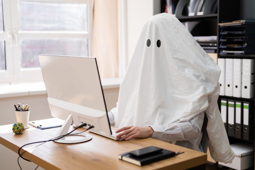 Person dressed as a ghost sitting at a desk using a computer, symbolizing what to do when your web designer ghosts you.