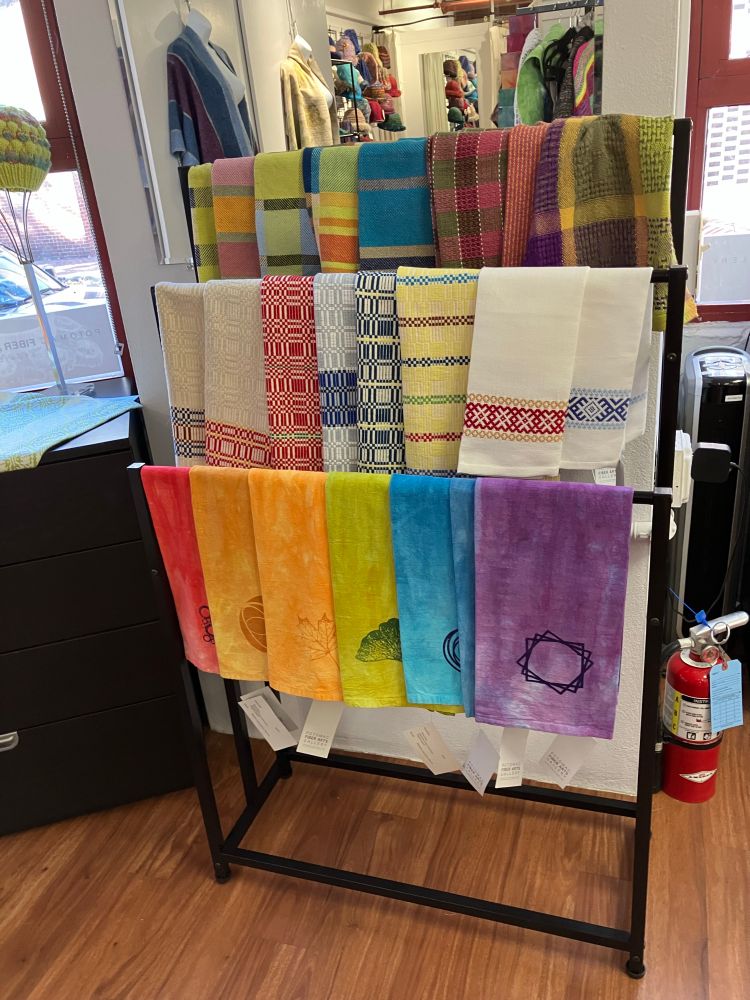 A rainbow of hand-dyed, block-printed and woven dish towels hanging on a rack